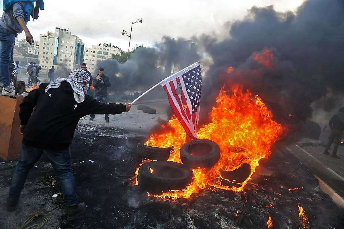 TOPSHOT - A Palestinian protester sets alight an America flag during clashes with Israeli troops at a protest against US President Donald Trump's decision to recognize Jerusalem as the capital of Israel, near the Jewish settlement of Beit El, near the West Bank city of Ramallah on December 7, 2017. / AFP PHOTO / ABBAS MOMANIABBAS MOMANI/AFP/Getty Images