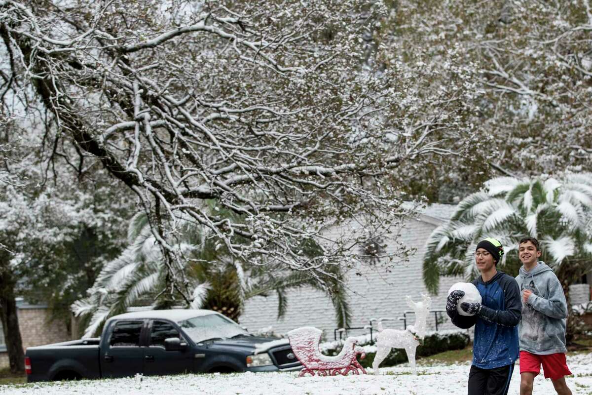 Tyler Hammett carries a large snowball as he and Noah Garcia run under snow-covered trees after the area saw snow fall overnight on Friday, Dec. 8, 2017, in Oak Ridge North, Texas.