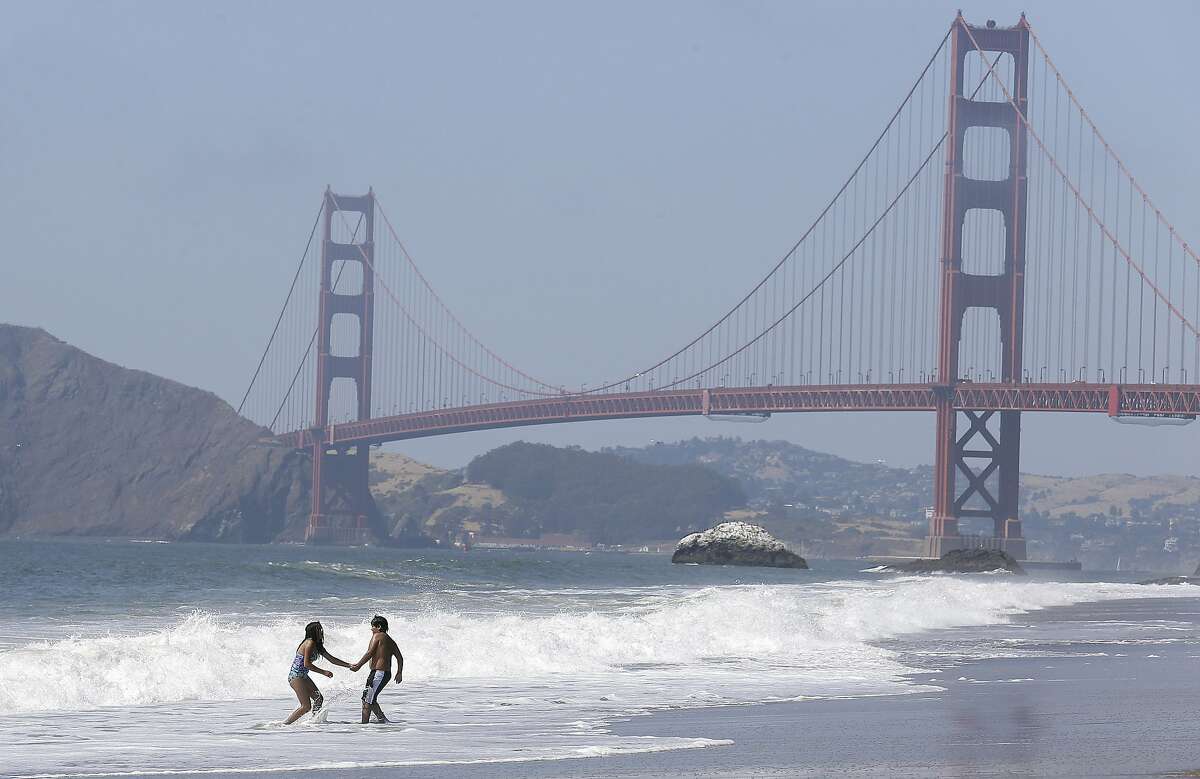FILE - This Wednesday, June 21, 2017 file photo children play in the surf at Baker Beach with the Golden Gate Bridge shown at rear in San Francisco. Engineers will have to do more wind testing on a model of the Golden Gate Bridge before the span is modified for a seismic upgrade project and a suicide barrier. Testing done last month in a Canadian lab showed the bridge model performed well under a horizontal wind flow of more than 100 mph. But the bridge became unstable when the wind flow was changed by 1 degree. (AP Photo/Jeff Chiu,File)