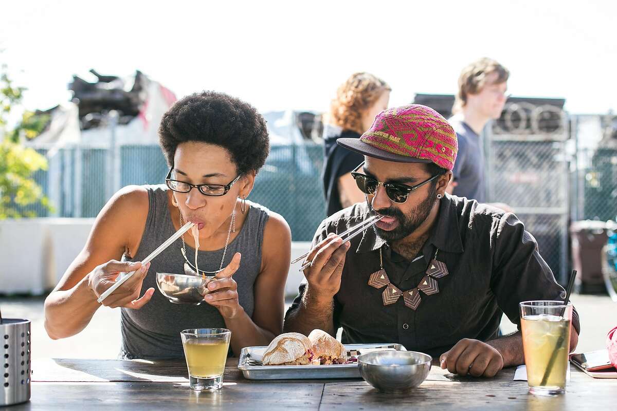 Jocelyn Jackson, of JUSTUS Kitchen, and Saqib Keval, of People's Kitchen, eat noodles and a sandwich during lunch at FuseBOX in Oakland.