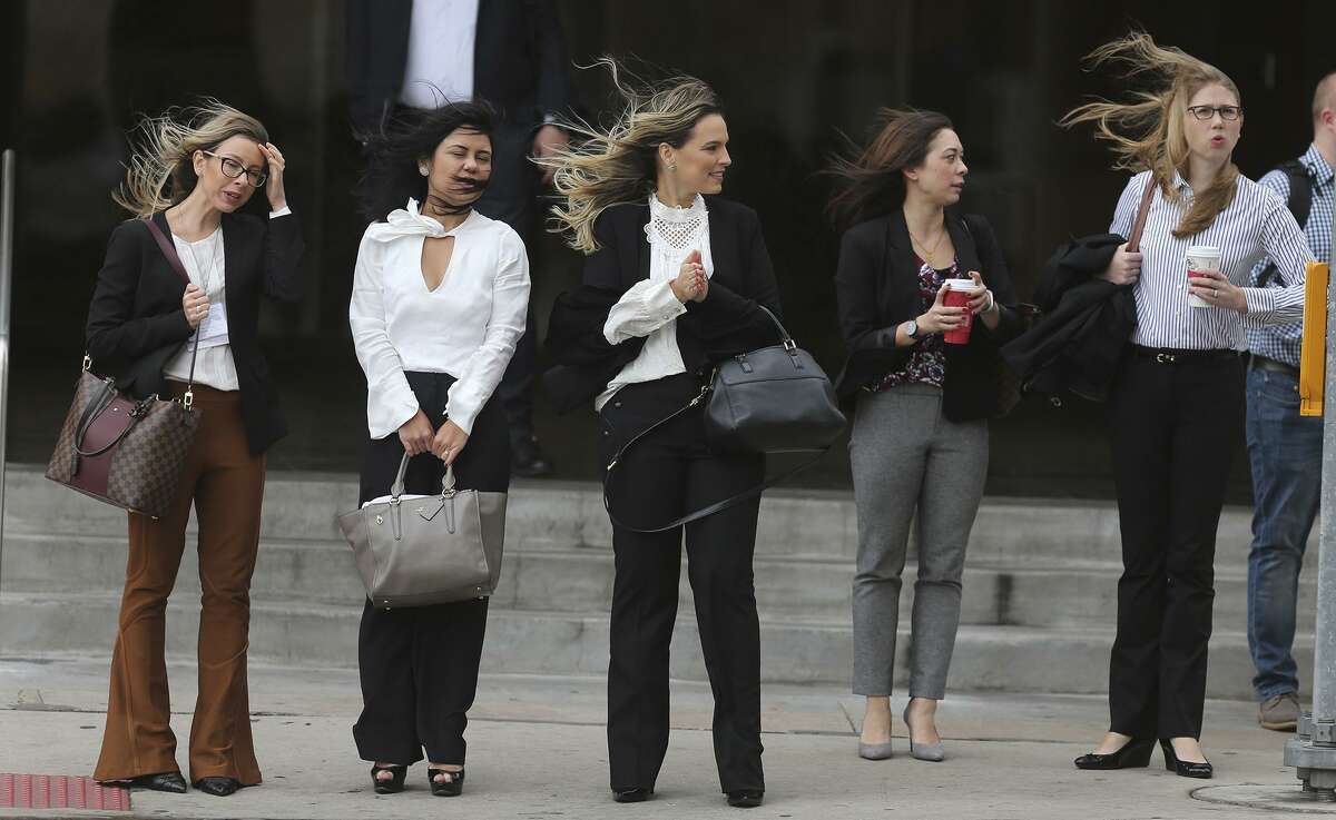 Pedestrians cope with windy weather conditions while walking downtown.