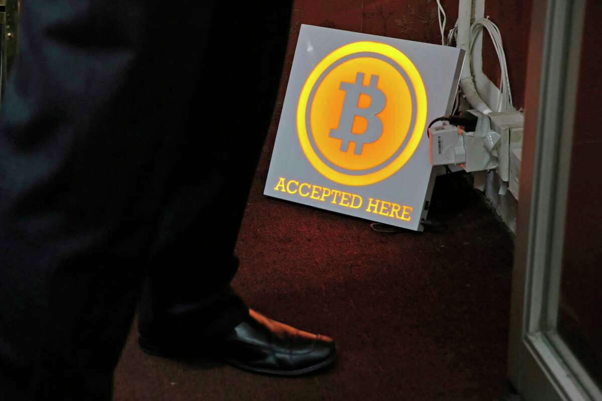 In this Friday, Dec. 8, 2017, photo, a man stands besides a Bitcoin sign near a Bitcoin ATM in Hong Kong. The launch of a U.S. futures contract for bitcoin on Sunday, Dec. 10, 2017, underscores the virtual currency's increasing mainstream acceptance, including in many parts of Asia, where it already has a wide following among speculators and investors. (AP Photo/Kin Cheung)