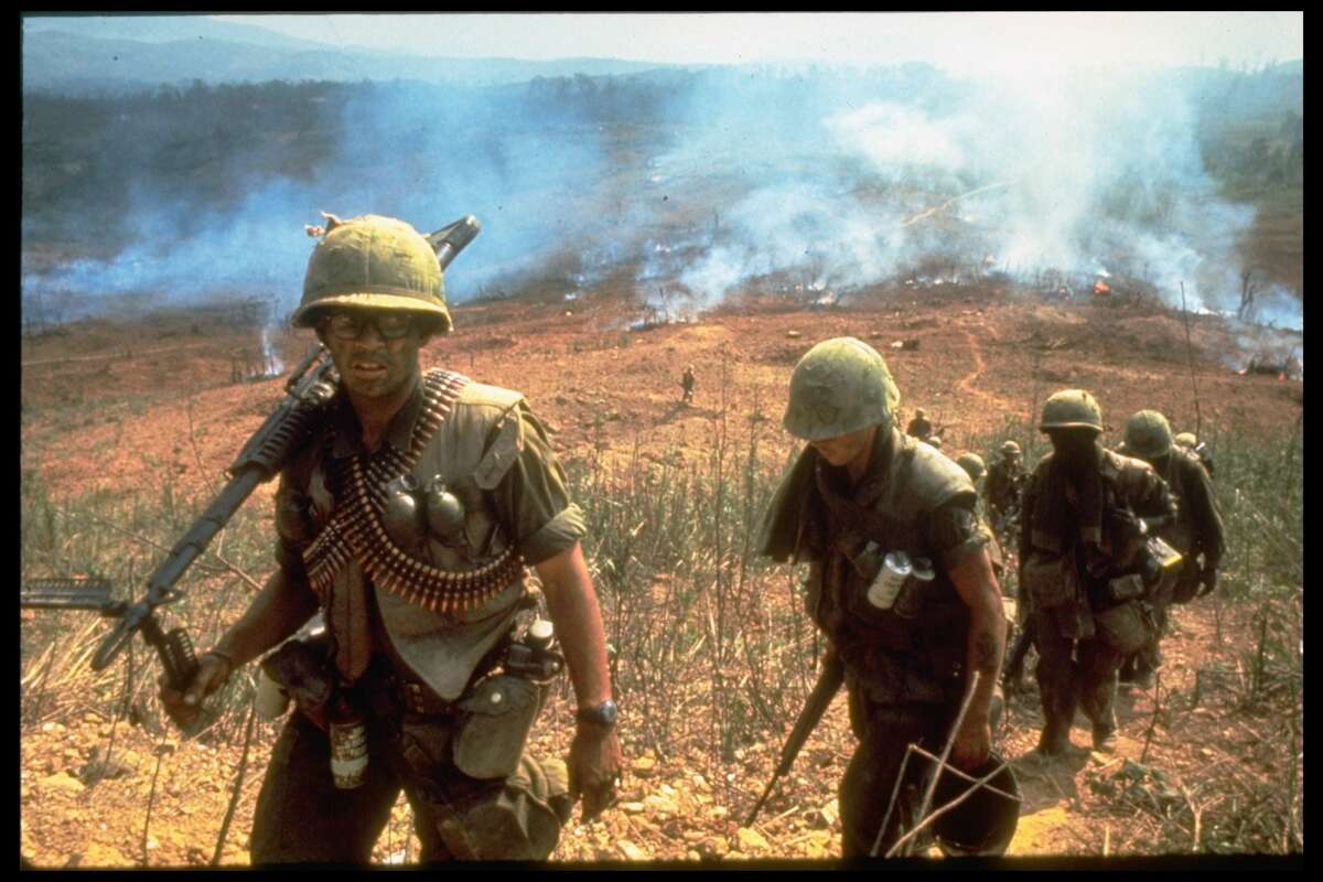 A line of American soldiers march up a hill during the Route 9 offensive while fires behind them send smoke into the air, Vietnam, 1968.