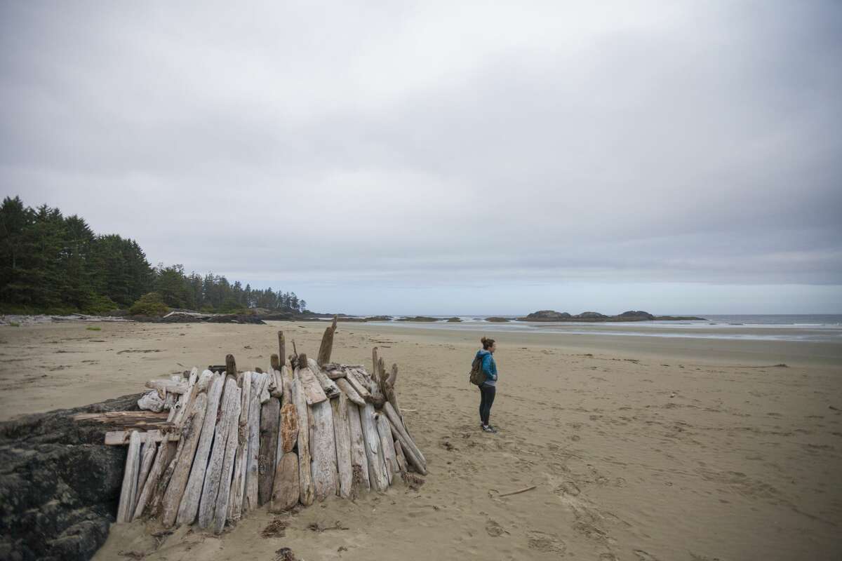 Young woman standing outside of a beach shelter made entirely out of driftwood on Wickaninnish Beach, Pacific Rim National Park, Vancouver Island, British Columbia.