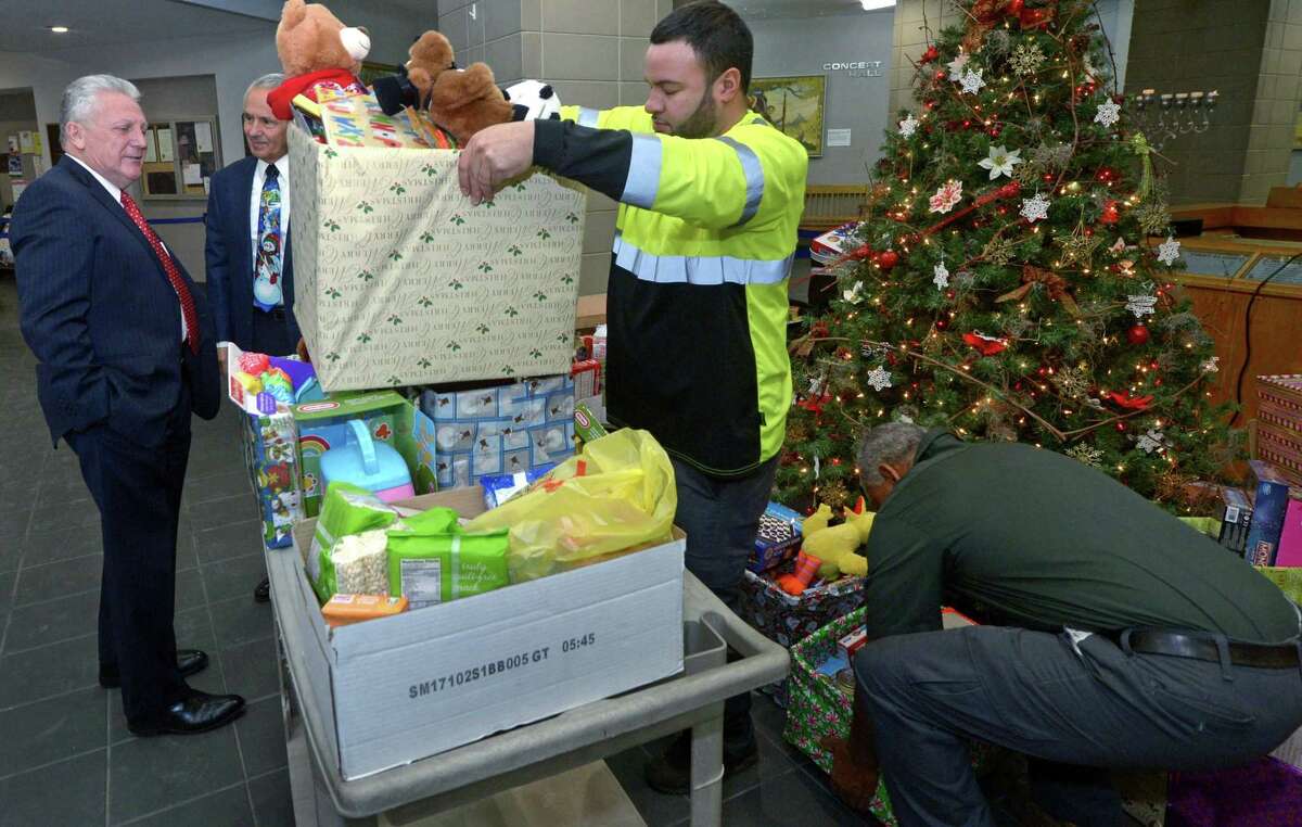 Mayor Harry Rilling watches as Department of Public Works employees Andrian Ibarrondo and Oliver Lawrence load up holiday gift baskets donated by city and Board of Education employees to be delivered to the Salvation Army, the Open Door Shelter and Person-to-Person as Corky Stewart, chairman of the Open Door Shelter Board of Directors, second from left, looks on Tuesday in the first-floor atrium of City Hall in Norwalk. City employees had filled the baskets with toys and non-perishable food for local families in need.