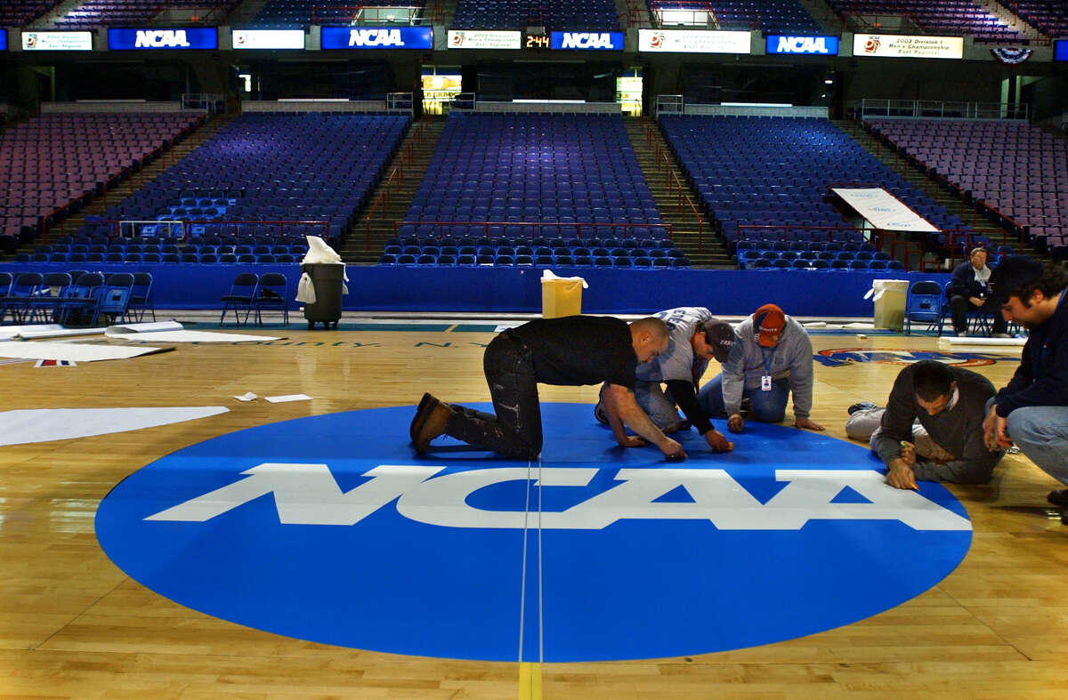 Pepsi Arena employees, from left to right; Jose Soler, Scott Wieczorkowski, Rick Lennox, and Nathan Sims (man at far right is unidentified) apply the finishing touches to a decal applied to center court at the Pepsi Arena on March 26, 2003, in Albany, N.Y., in preparation for this weekend's NCAA East Regional final in men's basketball. The decal has an adhesive, and will be removed at the tournament's end. (Philip Kamrass/Times Union)