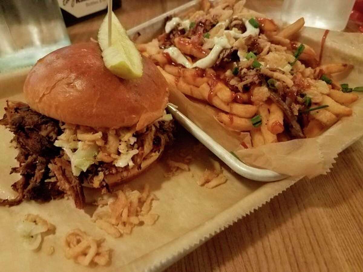 The Saginaw Joe Pulled Pork sandwich at Midland Brewing Company, 5011 N. Saginaw Road in Midland, is stacked high with coleslaw and crispy onions, and requires the use of a fork to finish off the meal. An order of Hog fries makes the meal complete. (photo by Matthew Woods)