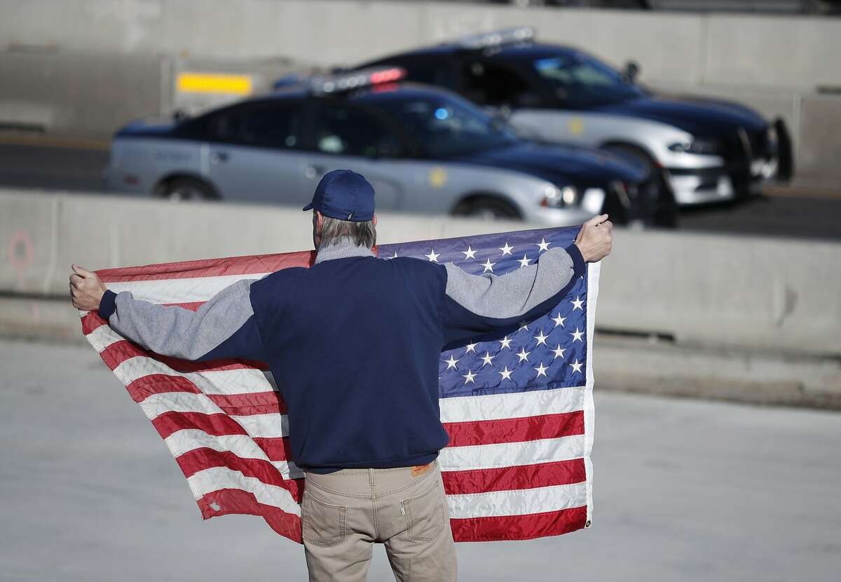 David Morgan of Highlands Ranch, Colo., holds an American flag as a procession of law enforcement vehicles accompany a hearse carrying the body of a sheriff's deputy shot and killed while responding to a domestic disturbance Sunday, Dec. 31, 2017, in Highlands Ranch, Colo. (AP Photo/David Zalubowski)