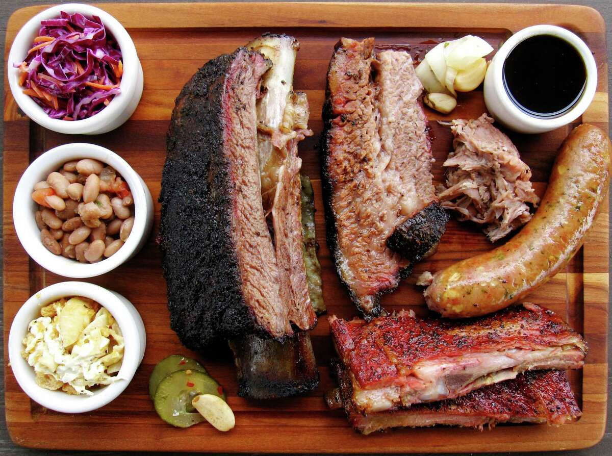 A cutting board full of barbecue and sides from 2M Smokehouse, including brisket, pork ribs, sausage, pulled pork, a beef rib, cole slaw, beans and chicharrón mac and cheese.