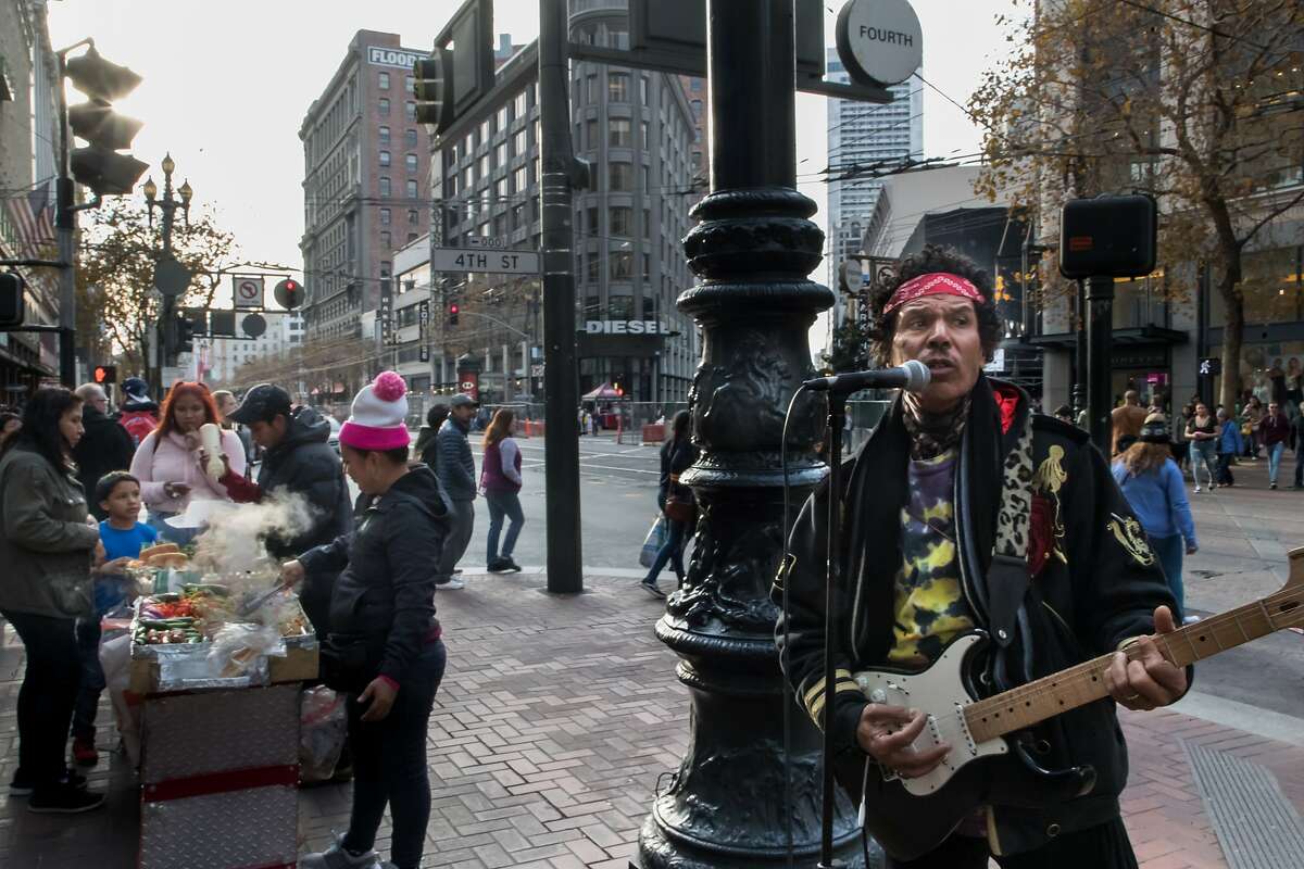 Robert Moses (right) asks the band with guitarist/vocalist Victor Hernanez to participate in The Bootstrap Project which will show street performers in February as they preform at Market Street on Saturday, Dec. 30, 2017 in San Francisco, Calif.