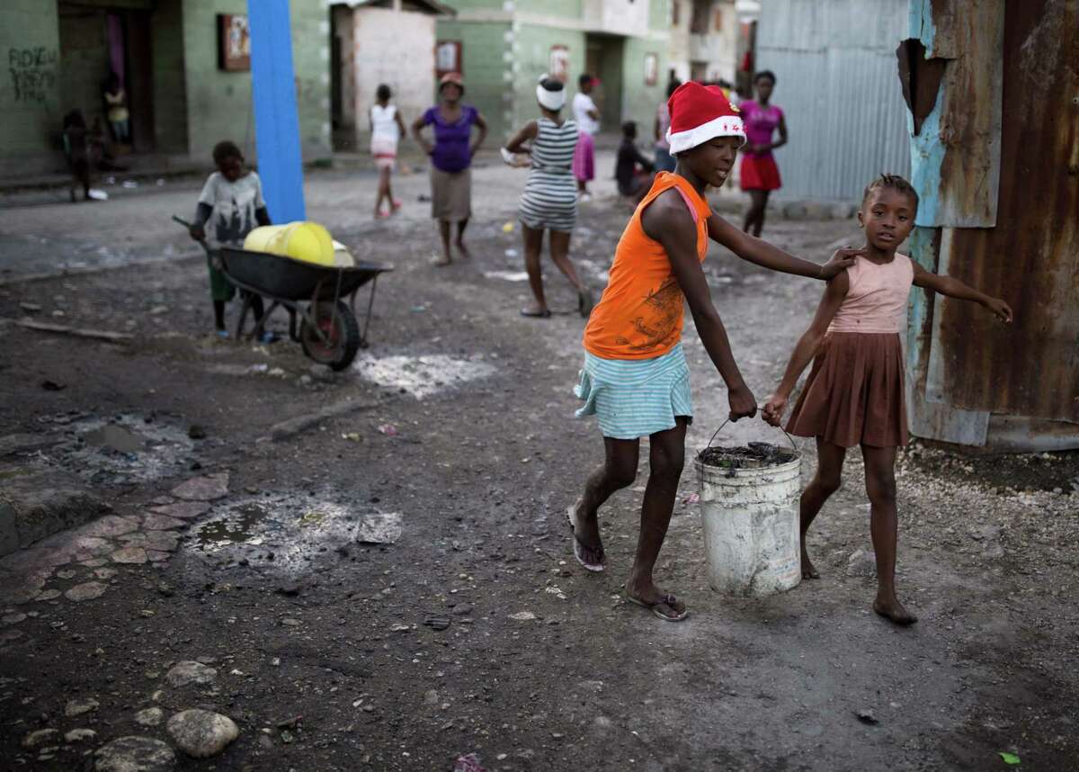 Children carry a bucket of trash to a dump in a Port-au-Prince, Haiti, slum. The inability of poverty-stricken parents to adequately feed and educate their children has made Haiti a hub for human trafficking.