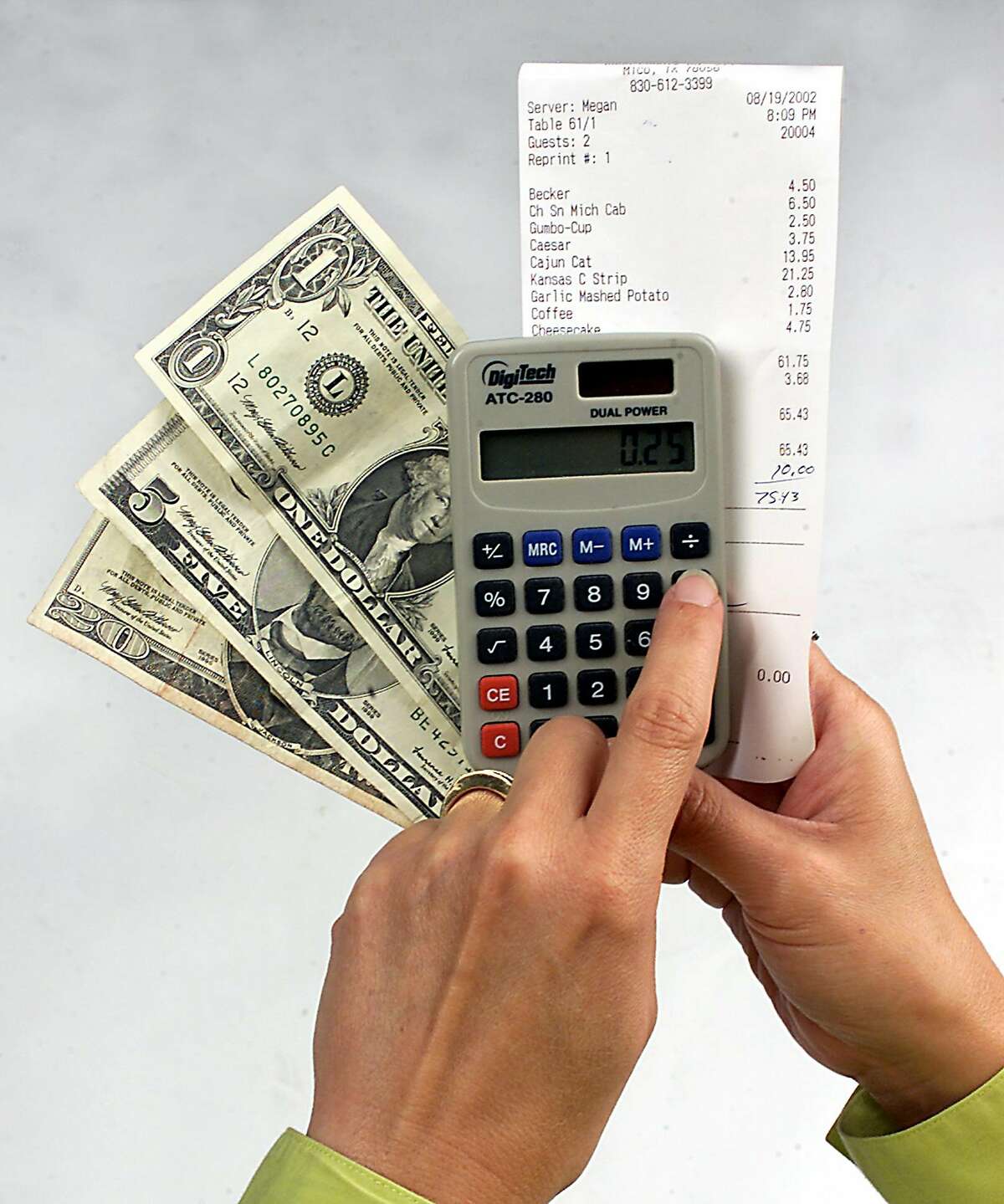 Hands using a calculator to figure a tip while holding money and a receipt. PHOTO BY JUANITO GARZA / STAFF