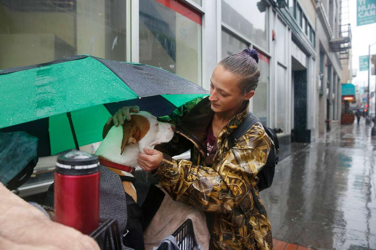 Amber Fina, who is homeless, checks on her dog, Ganja, as they stand on Grove Street before taking shelter from the rain in Burger King on Monday, January 8, 2018 in San Francisco, Calif.