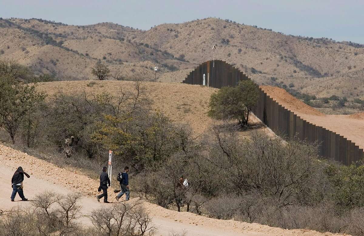 Migrants walk toward the U.S.-Mexico border wall on the outskirts of Nogales, Mexico, Tuesday, April 1, 2008. U.S. officials say the Bush administration will bypass more than 30 laws and regulations in an effort to complete 670 miles (1,050 kilometers) of fence along the U.S. border with Mexico by the end of this year. (AP Photo/Guillermo Arias)
