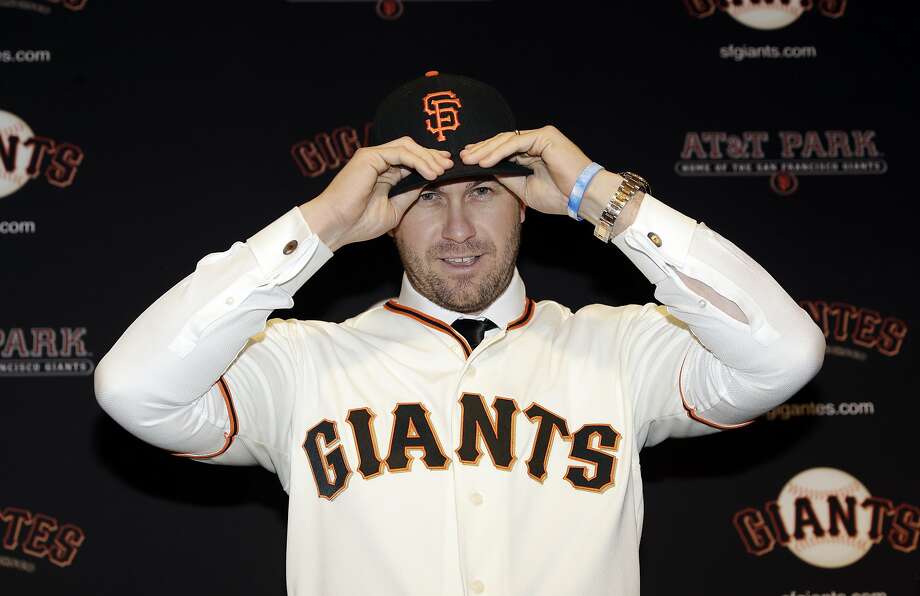 San Francisco Giants' Evan Longoria puts on a team hat and jersey during his introductory press conference at AT&T Park on Friday. He will wear No. 10. Photo: Marcio Jose Sanchez, Associated Press