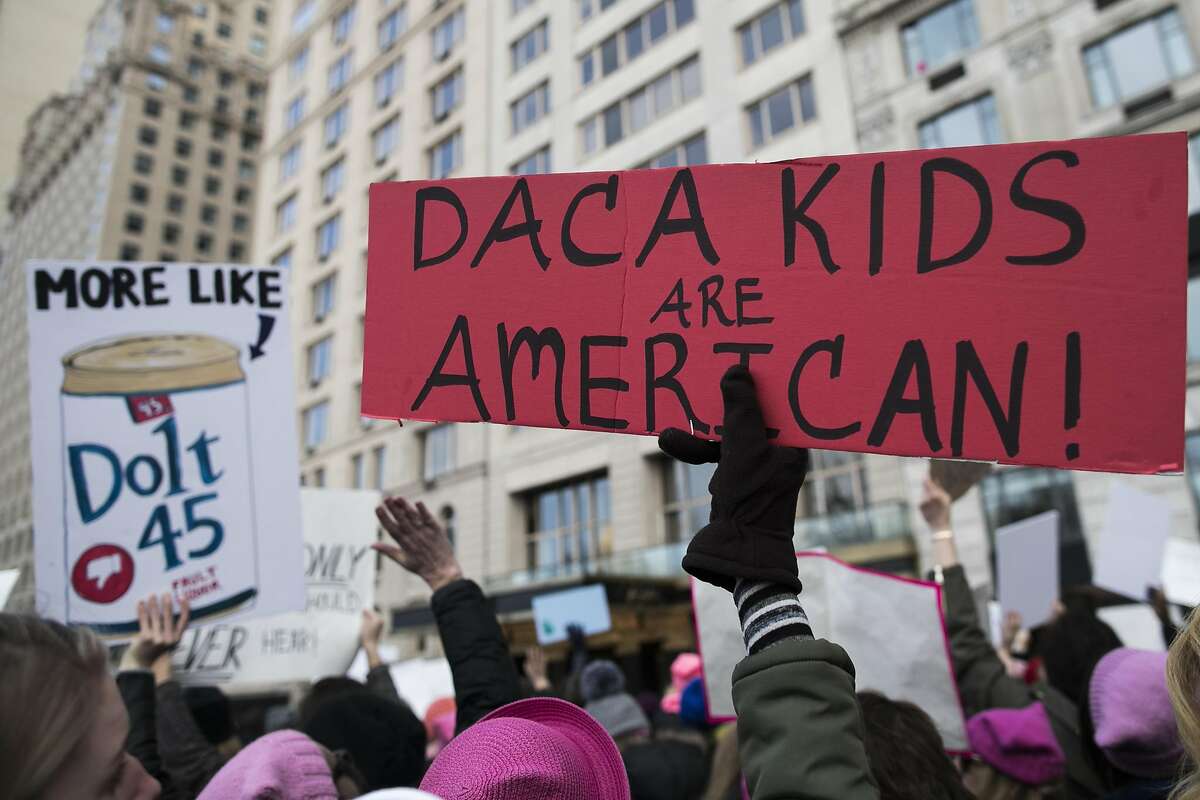 A demonstrator holds a sign that reads "DACA Kids Are American" at Columbus Circle during the Women's March on New York City in New York, U.S., on Saturday, Jan. 20, 2018. One year after the inauguration of President Donald Trump, thousands of people will again gather to protest for equal rights at the 2018 Women's March. Photographer: Jeenah Moon/Bloomberg
