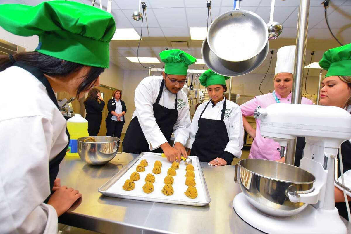 Klein Forest students Emily Martinez, Alan De La Rosa and Dayanara Moreno put down the cookie dough on the cookie sheet for baking AS Instructed by chef Jennifer Rodgers And viewed by student Lourdes Menjivar.