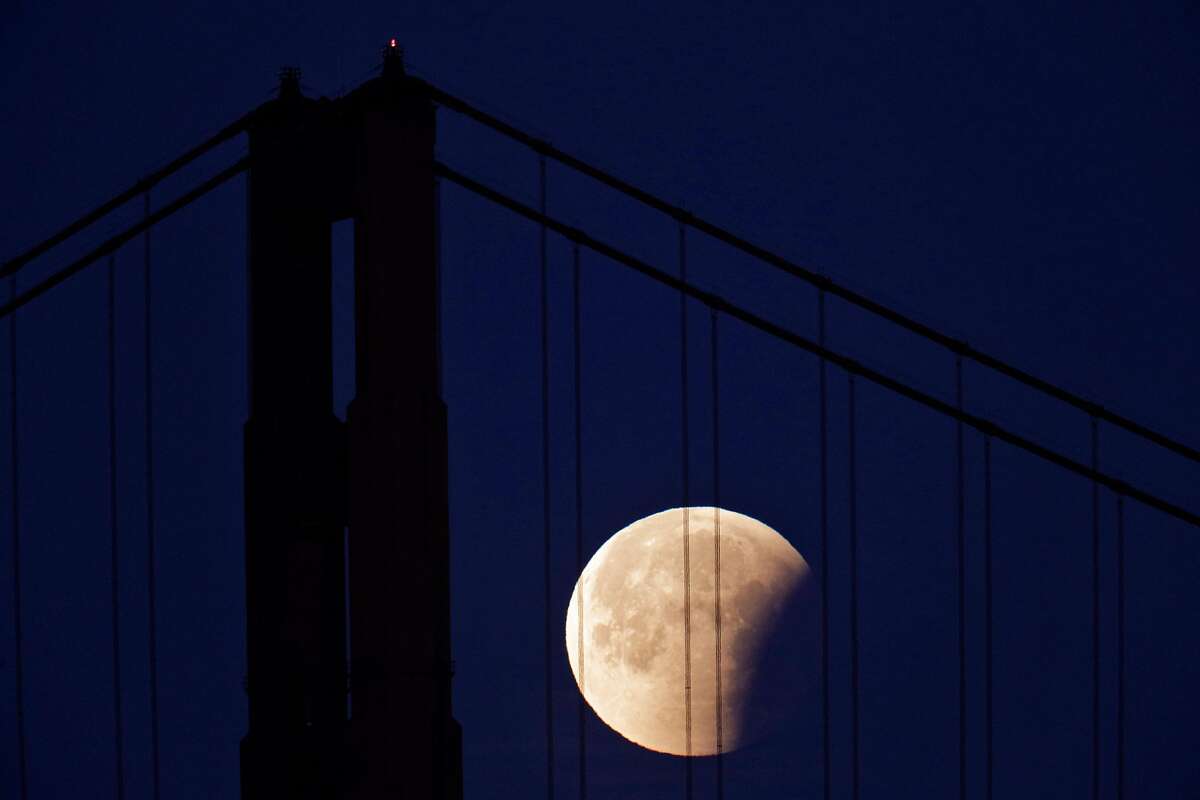 The partially eclipsed “super blue blood moon” is seen behind the Golden Gate Bridge on Jan. 31, 2018, in a view from the San Francisco Yacht Club.