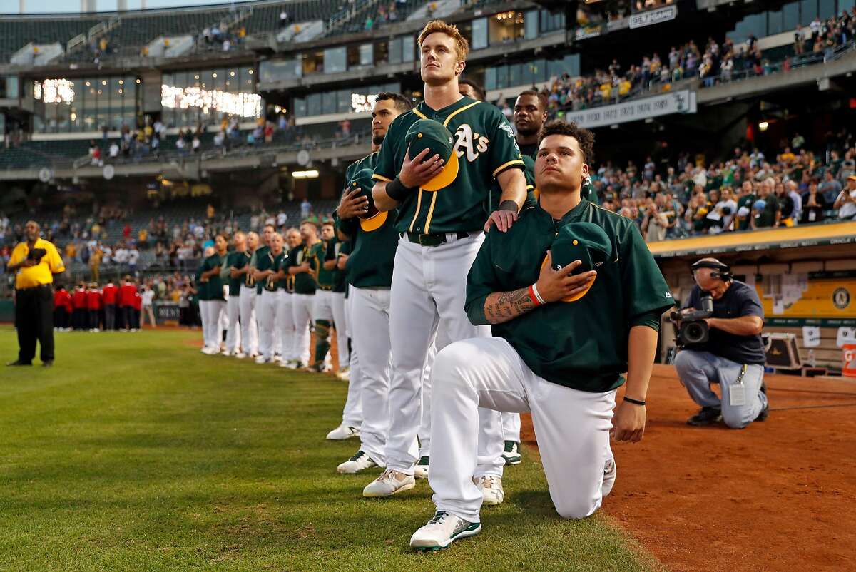 Oakland Athletics' Bruce Maxwell kneels during the National Anthem as teammate, Mark Canha, flanks him before A's play Seattle Mariners' during MLB game at Oakland Coliseum in Oakland, Calif., on Tuesday, September 26, 2017.
