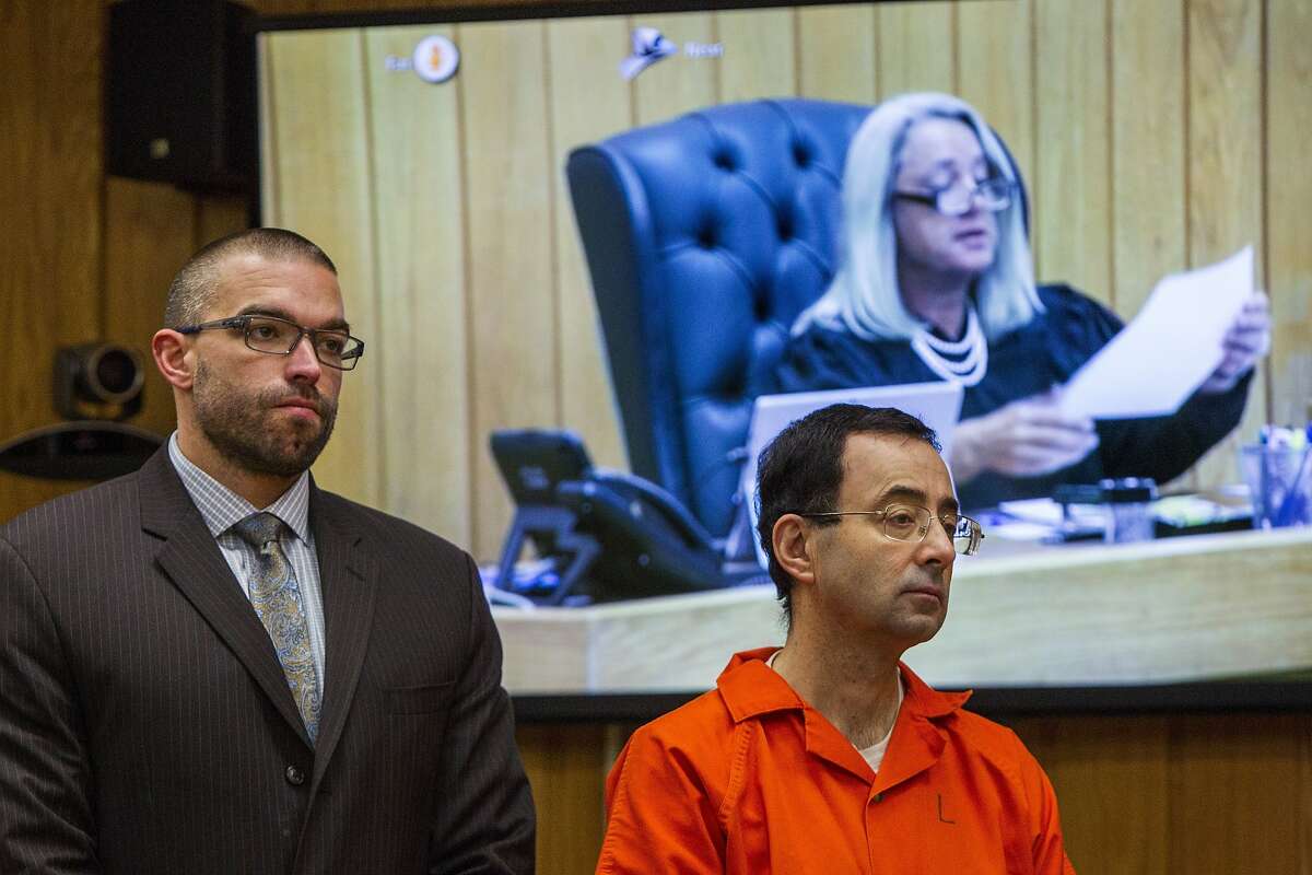 Larry Nassar, right, listens near defense attorney Matthew Newberg as Judge Janice Cunningham (pictured on the monitor) sentences Nassar at Eaton County Circuit Court in Charlotte, Mich., Monday, Feb. 5, 2018. Michigan State University has reached a $500 million settlement with hundreds of women and girls who say they were sexually assaulted by sports doctor Larry Nassar in the worst sex-abuse case in sports history.
