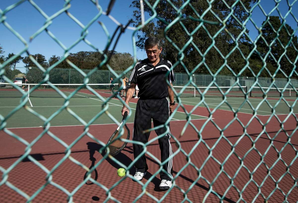Michael Fujimoto, 73, of San Francisco is seen through a hole in the fence as he retrieves a ball while playing a match with friends at the Golden Gate Park Tennis Center. Fujimoto has been using these courts regularly for over 50 years.