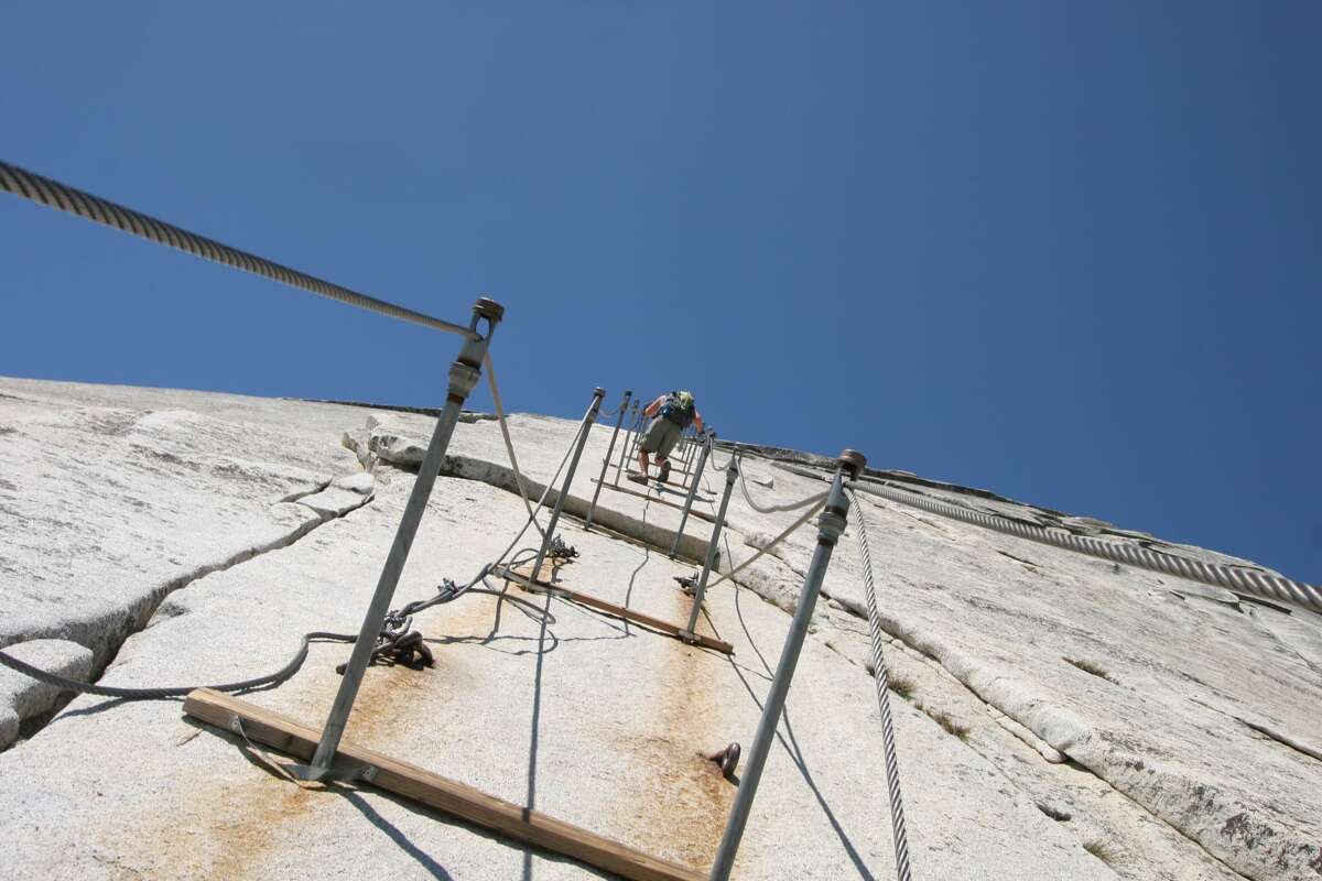 Hiker nearing the peak of Half Dome. Cables are clearly visible, as well as sheer cliff