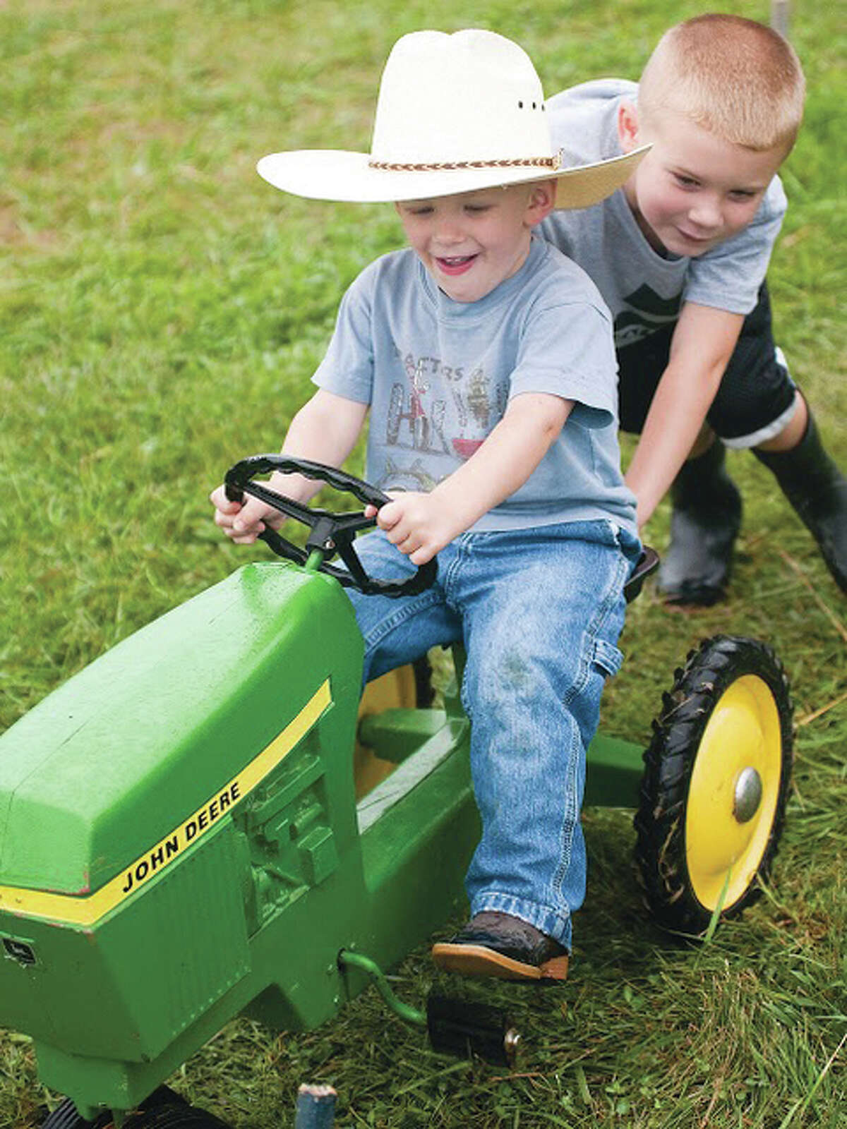 Joshua Cordes, 5, pushes his younger brother, James, on a miniature John Deere tractor Sunday at the silver anniversary of the Tri-County Antique Club’s Olden Days Festival in Dow.
