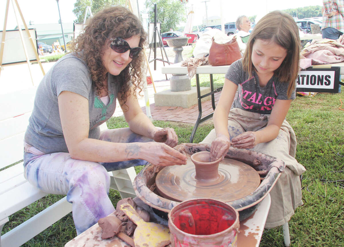 Madelyn Plummer, 7, of Alton, tries using a potter’s wheel with some help from Susan Elmendorf of the Jacoby Arts Center during a demonstration at “Art in the Park,” a two-day art fair in The Grove Memorial Park in Grafton Sunday afternoon. More than three dozen artists had works on display at the fair, now in its ninth year.