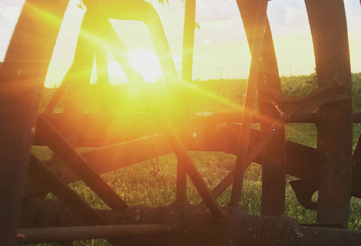 The light of the setting sun reflects off an old Oliver planter sitting in a field.