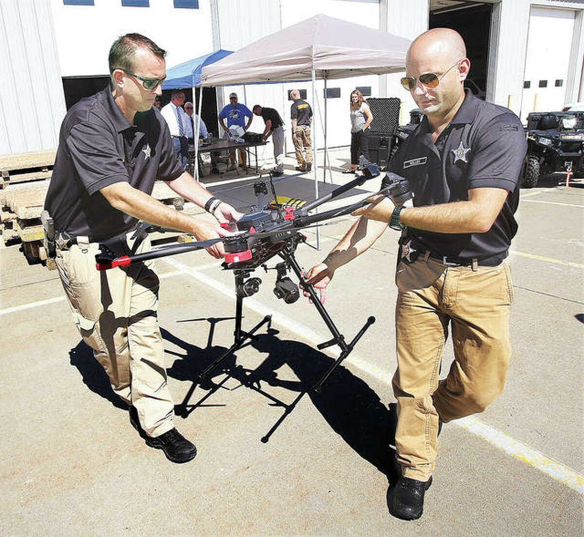 Madison County Sheriff’s Deputies Darren Onwiler, left, and Bob Weller, right, carry the Sheriff Department’s new drone, which has retractible landing legs, into the clear to launch it Tuesday. While regulations limit the height of flight to 400 feet in the air, the drone is capable of much higher altitudes.