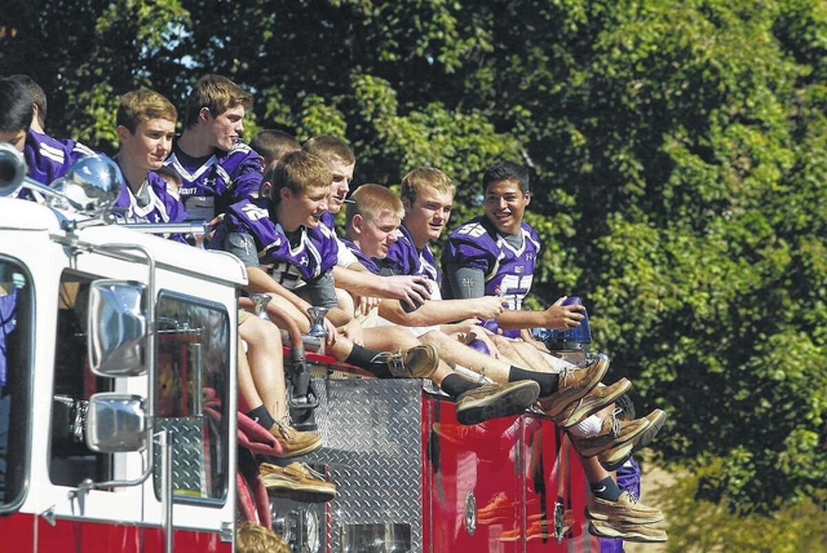 Members of the Routt Catholic High School football team toss purple mini-footballs and candy to children during the school’s homecoming parade Friday.