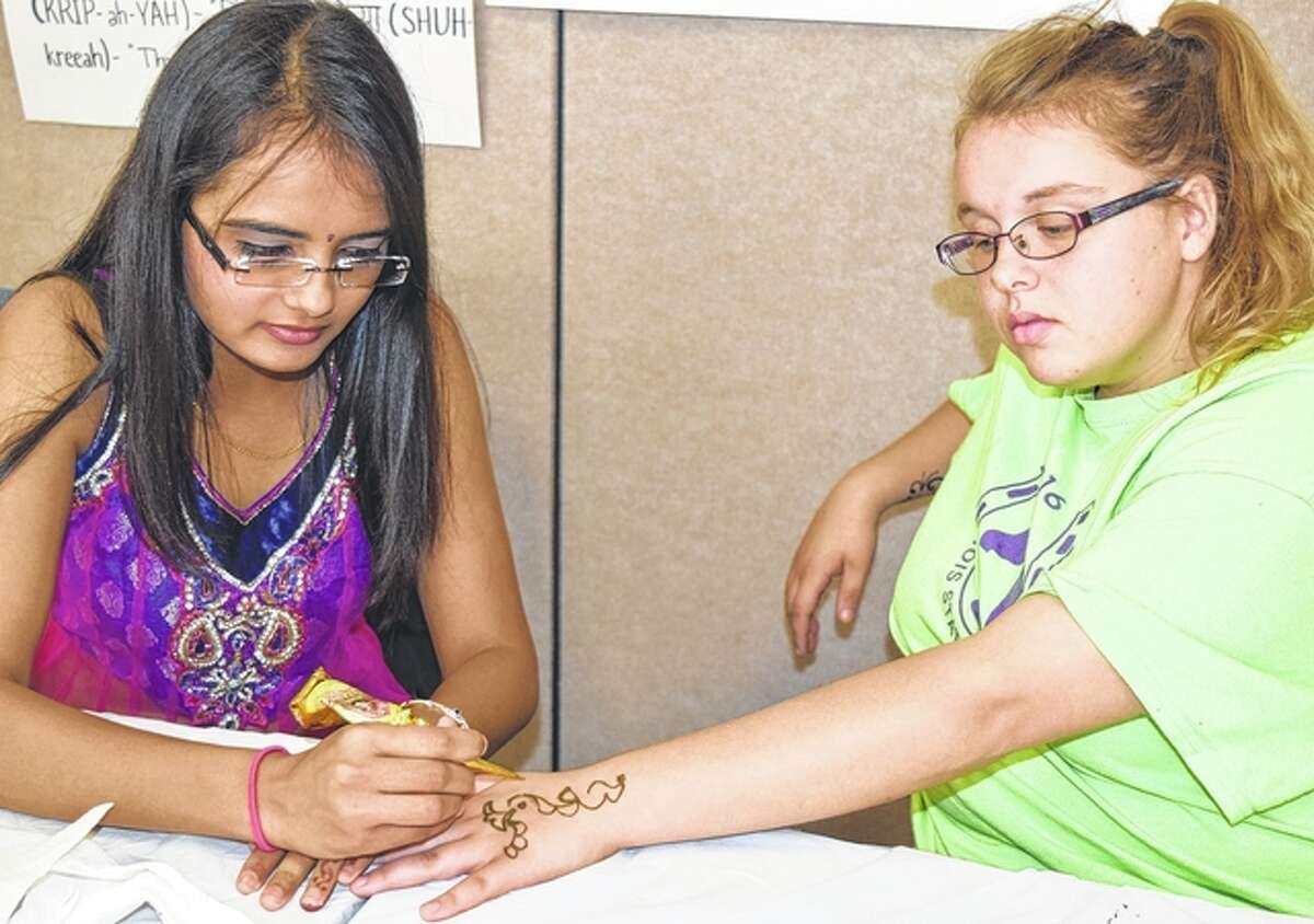 Aditi Shah (left) draws a design on Morgan Lonergan’s hand using henna during the Multicultural Fair at Lincoln Land Community College in Jacksonville on Thursday.