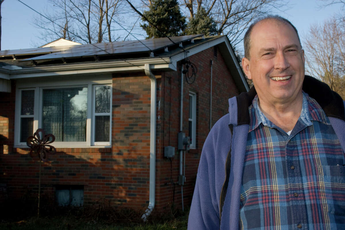 Mark Stewart stands next to his Godfrey home, which now supports an array of solar panels, nearly eliminating his summer electric bill.