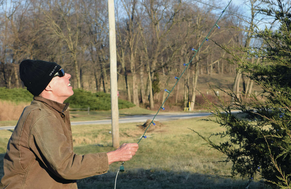 Jonn Herzberger stretches a string of lights that was hung on a tree along Route 125 in Bluff Springs.