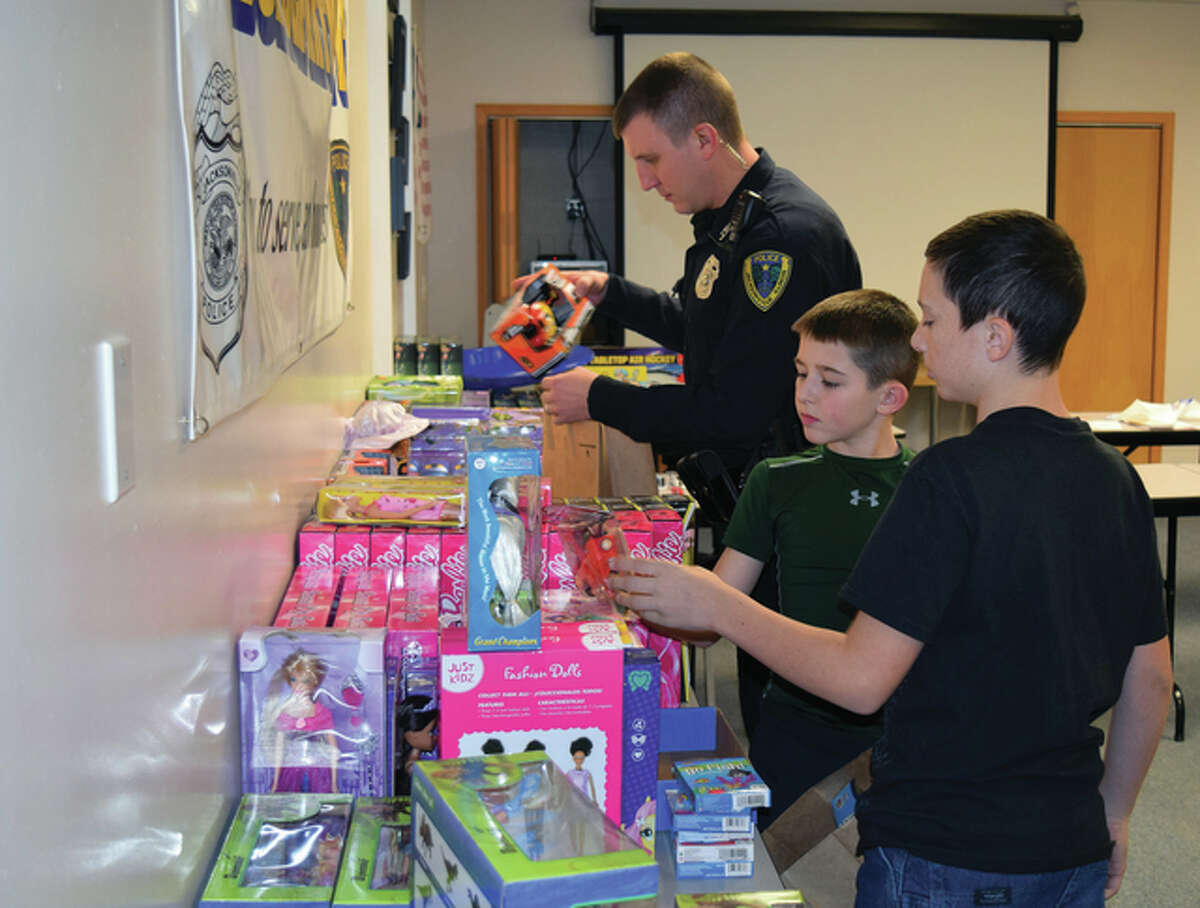 Jacksonville Police Department Patrolman Brad Long (from left), 10-year-old Declan Lahey and 11-year-old Kohen Hoots bag toys Wednesday for distribution. The toys and other items were purchased with money from the Nichols Foundation trust fund, which annually provides Christmas gifts for less-fortunate Jacksonville children.