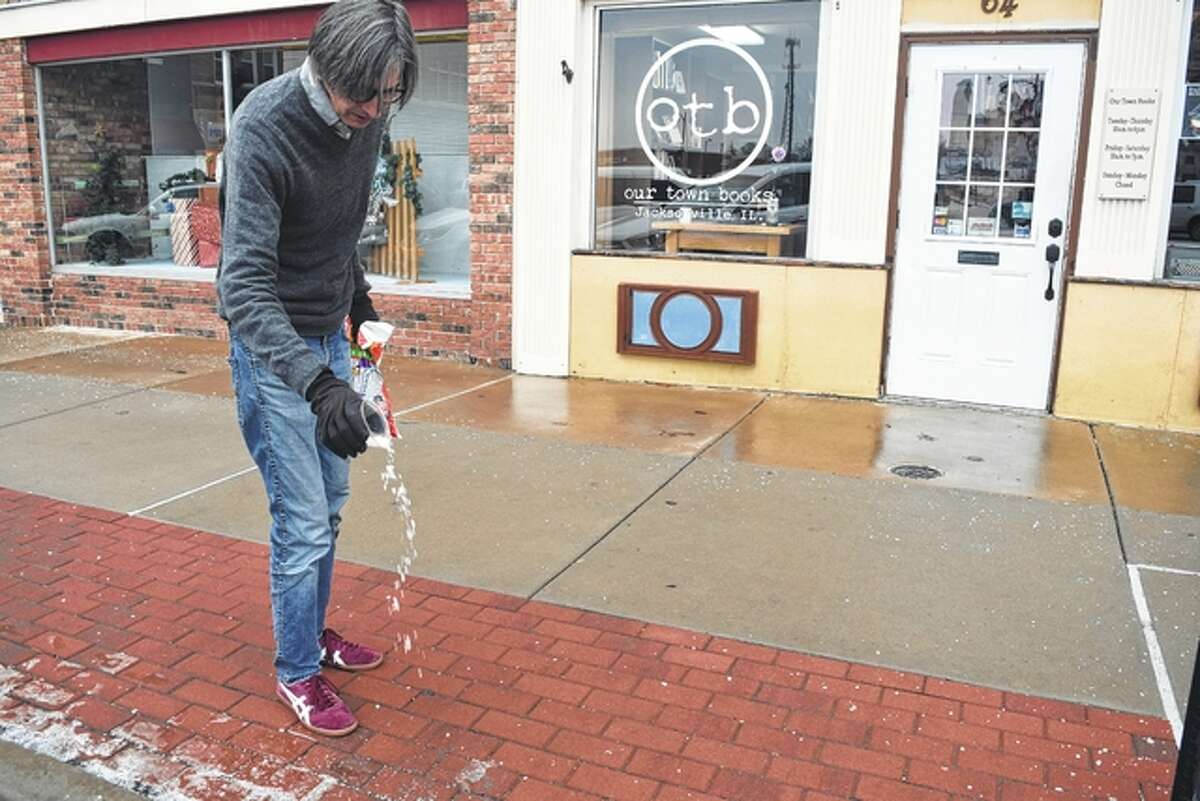 Our Town Books owner Andy Mitchell sprinkles ice melt Saturday on the sidewalk in front of his business on the east side of Jacksonville’s downtown square. The Jacksonville area received a thin coating of ice Friday and Saturday, while some areas to the west and south saw more significant accumulation.