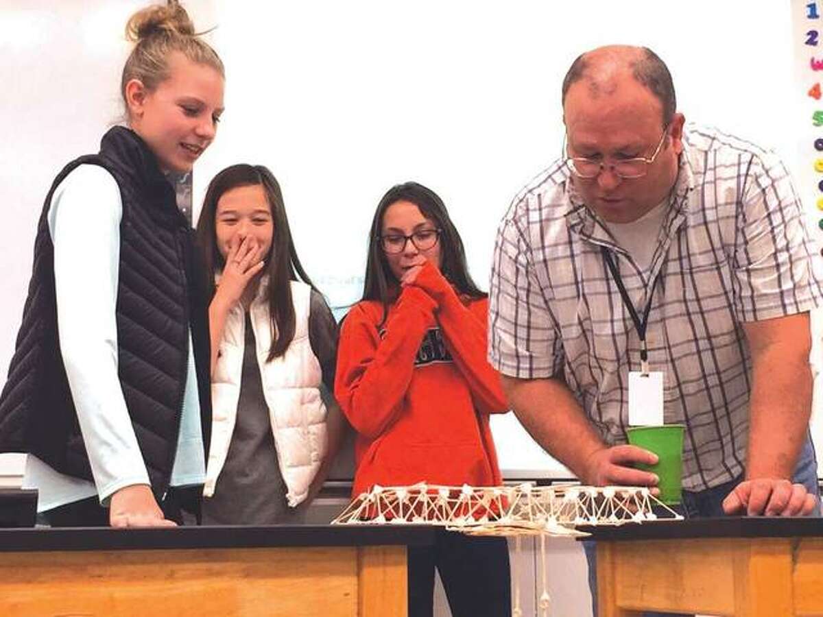Students Ella Cook, Maranda Fosse and Jocelynn Mercer watch with teacher Gardner Holland to see if their toothpick bridge will hold the necessary weight.
