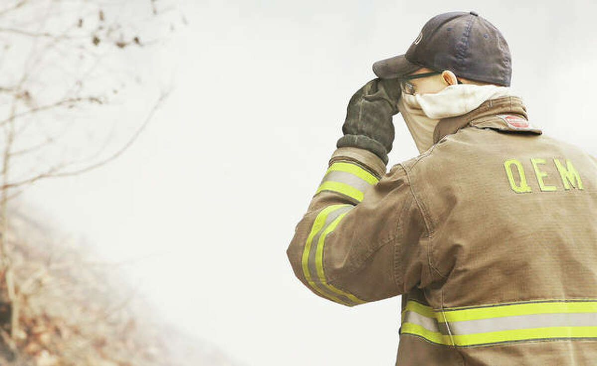 A QEM Fire Protection District firefighter pulls his neck covering up over his nose Thursday to lessen the smoke he was breathing in from a fire burning the bluffside on the Great River Road about two miles west of Lockhaven Road in Jersey County. The fire, swept by winds from the river, has been burning for days.