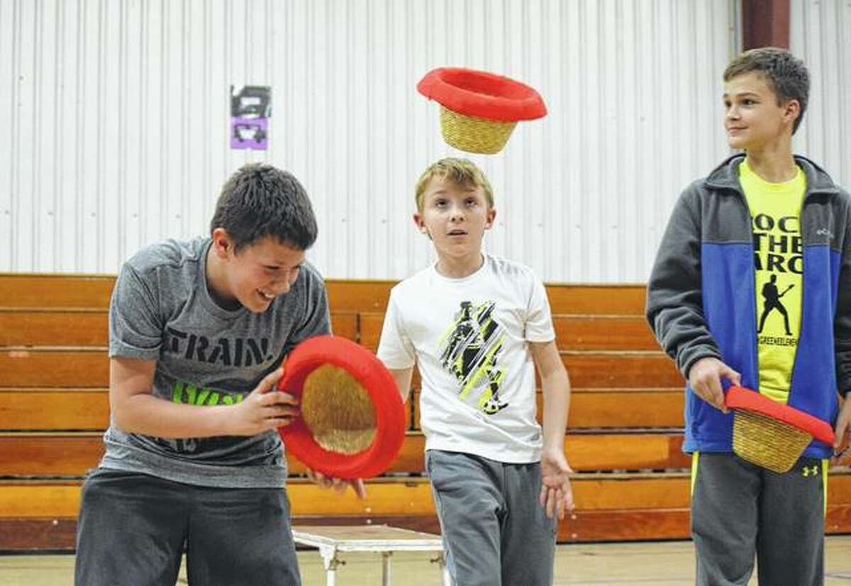 Sixth-graders Landon Fricke (left), Michael Rollins and Warren Legg attempt to flip a hat onto their heads during an assembly where the Fabulous Chinese Acrobats performed on Tuesday.
