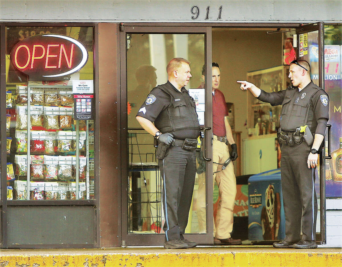 Alton Police officers and detectives talk in the doorway of the Conoco station at 911 College Avenue on State House Square, also known locally as the circle, Friday morning following a robbery of the establishment.
