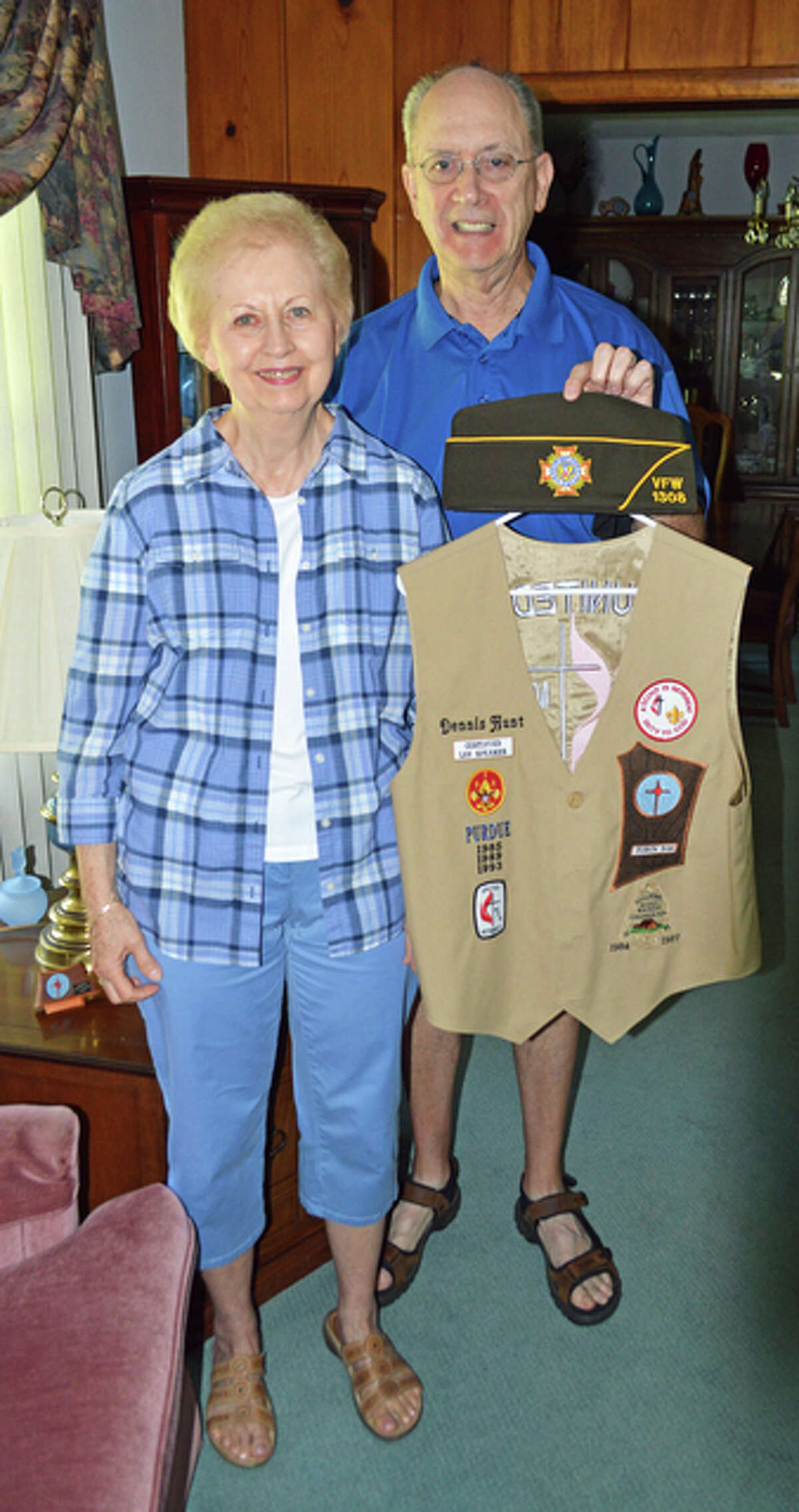 Dennis, holds his United Methodist Men vest and his VFW 1308 hat, with his wife, Sharon, in their East Alton home.