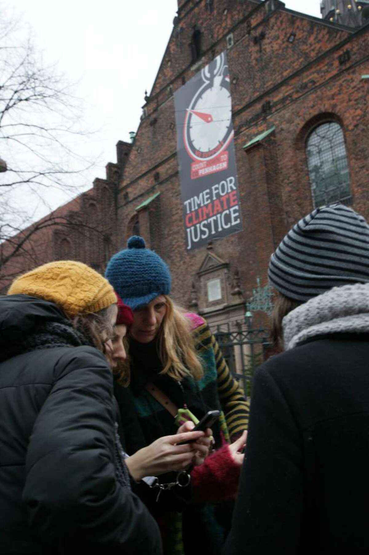 Four women look at the pictures they took of a poster displayed on a church reading "Time for Climate Justice" in the center of Copenhagen, Denmark, Sunday Dec. 6, 2009, one day before the Climate Summit kicks off. (AP Photo/Peter Dejong)