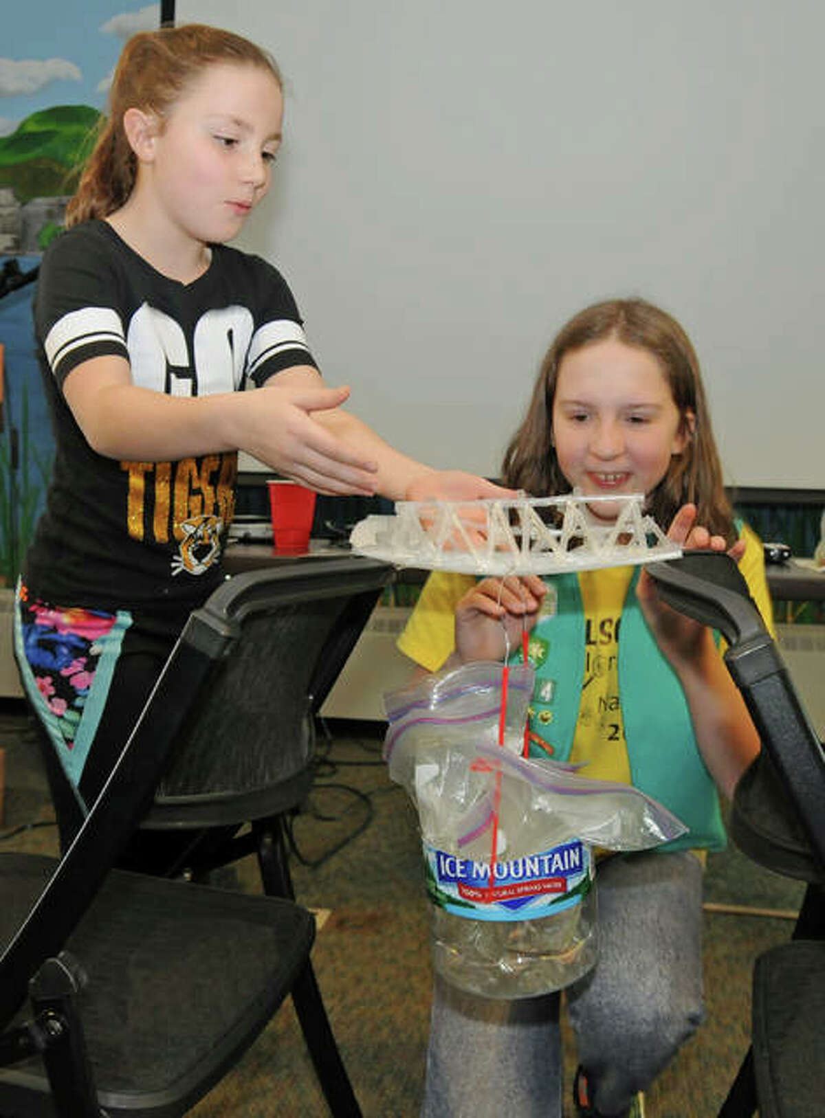 Mata Henfling, left, and Macie Myers, of the Worden Girl Scouts, test the strength of the plastic straw bridge they built during Saturday’s Building Bridges Merit Badge session.