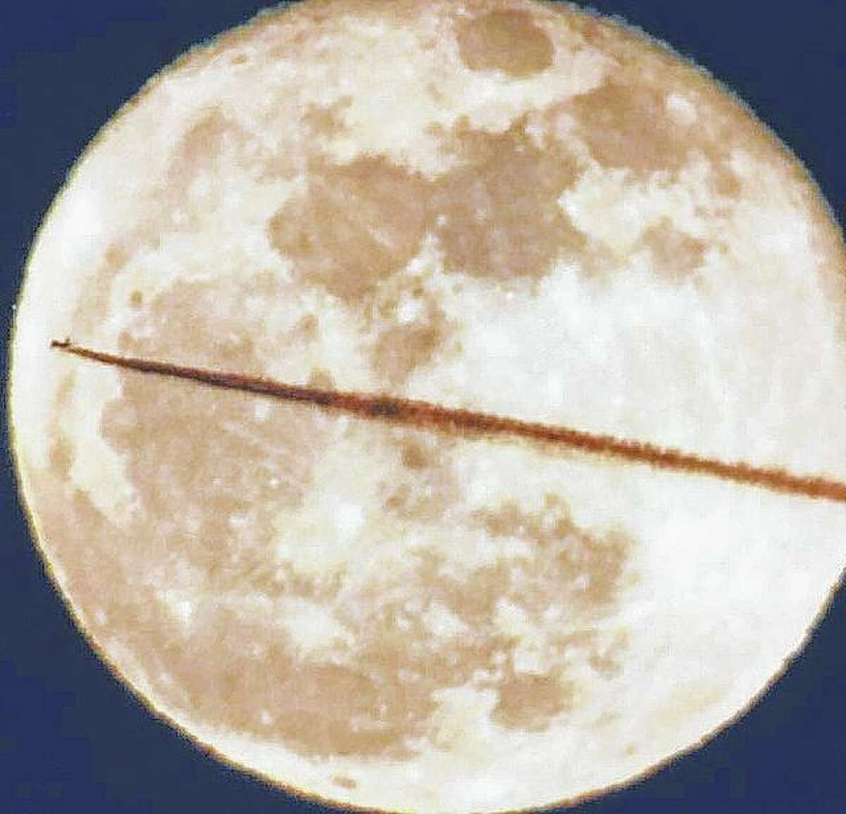 The vapor trail from a jet seems to cut a slice through the full moon.
