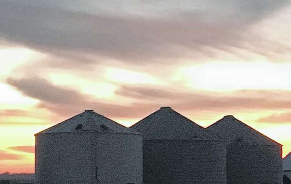The sun sets over grain bins, casting a golden hue across the sky.