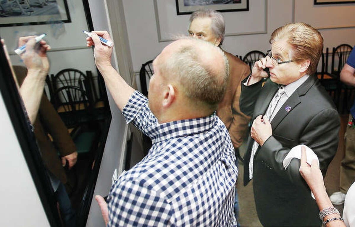 Alton Fire Chief Bernie Sebold, left, writes election returns on a mirror in a private room at Johnson’s Corner in Alton Tuesday night as Alton incumbent mayor Brant Walker, right, takes a phone call while numbers from the election roll in. Though unofficial until write-in votes are counted, likely late Wednesday or early Thursday, Walker won re-election by a wide margin, defeating challenger Scott Dixon and write-in candidates Dan Rauschkolb and Joshua Young.
