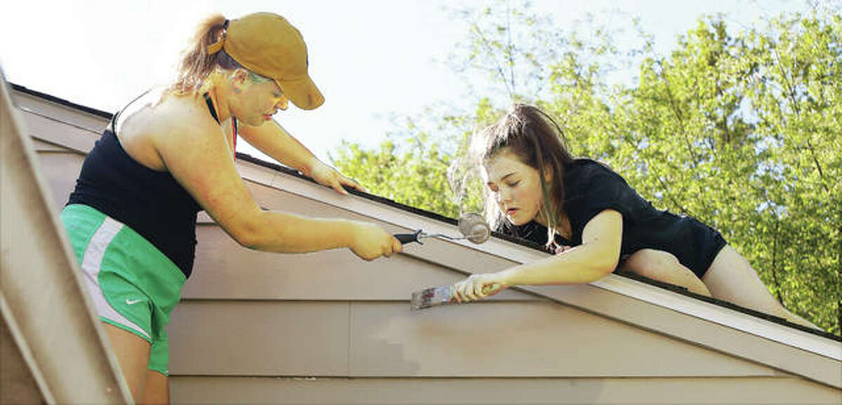 John Badman|The Telegraph Seniors from Marquette Catholic High School in Alton, like Abby Simonds, left, and Audrey Zigrang, were performing duties on Senior Service Day by painting near the roofline of a house in the 4100 block of Aberdeen Avenue in Alton. Marquette students were painting houses in both Alton and East Alton.