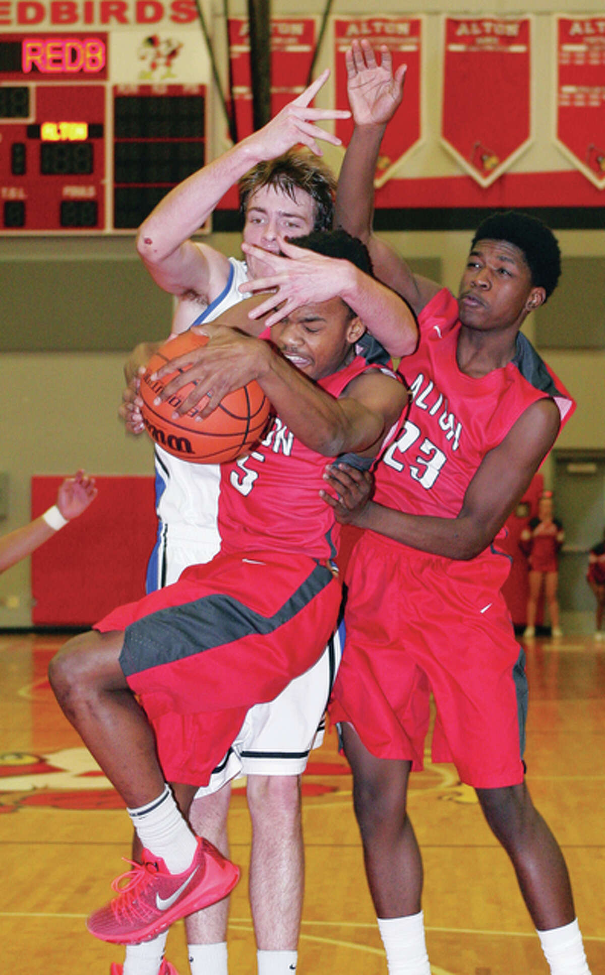Alton’s Jordan Golley (front) beats Quincy’s Garrett Gadeke (back left) and Kevin Caldwell (right) to a rebound Friday night at Alton High.