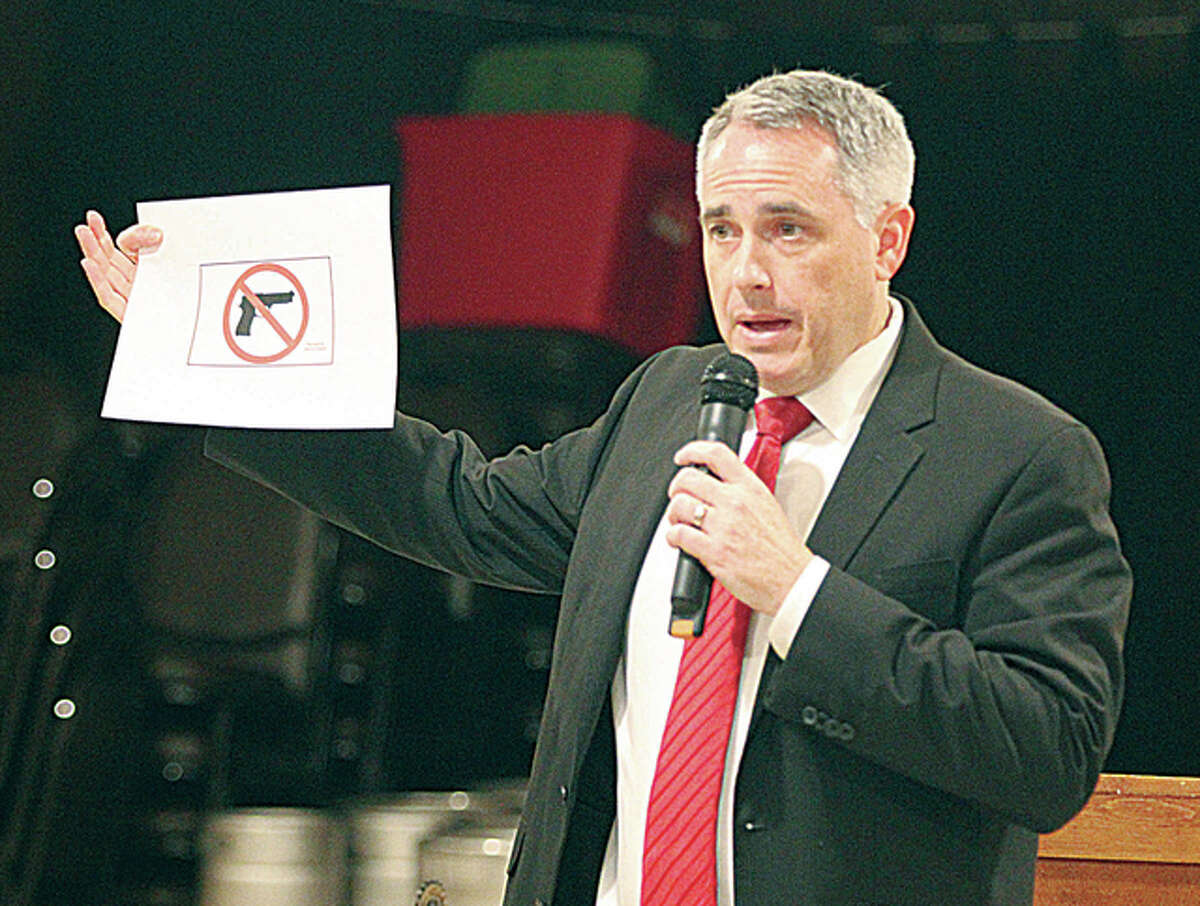 Madison County State’s Attorney Tom Gibbons holds a copy of the “magic sign” that must be displayed to prohibit people with concealed carry permits from taking firearms into a building. He noted that the law requires the sign to be an exact shape and size. Gibbons was talking about the state’s concealed carry license law at a meeting of the Alton-Godfrey Rotary Monday evening.