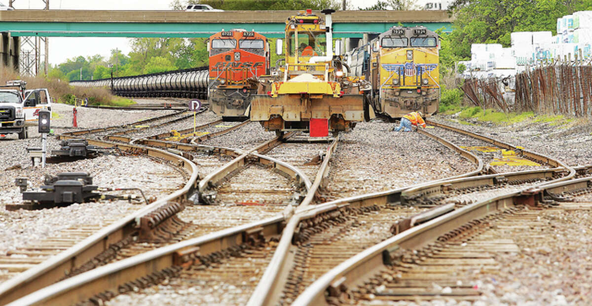 Less than a quarter of a mile from the tower, a worker kneels in front of a freight engine to perform work on the tracks. The area is criss-crossed with tracks and sidings in a very busy area for several railroad companies.